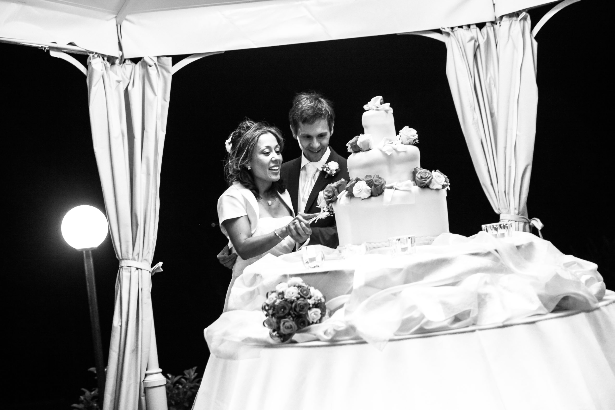 Claudia & Domenico schneiden die Hochzeitstorte an in schwarz/weiß